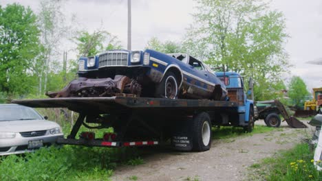 Ein-Ford-Torino-Aus-Den-1970er-Jahren-Steht-Auf-Der-Ladefläche-Eines-Pritschenwagens,-Umgeben-Von-Schrottautos