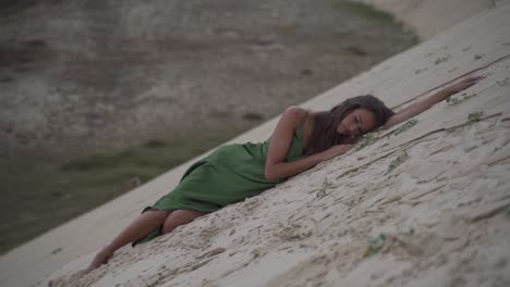 Women-in-an-elegand-classy-green-dress-laying-exhausted-in-a-desert-sand-dune-beach