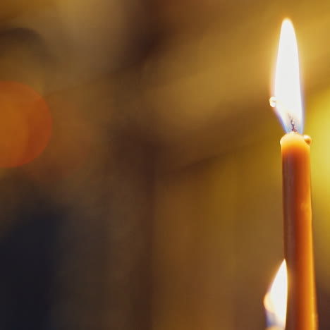 one candle is glowing brightly in church. golden light of candle flame. burning candle is the symbol of spirituality. close-up.