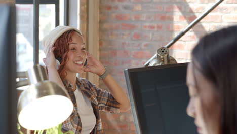 woman wearing headphones discussing project with colleague at modern office desk
