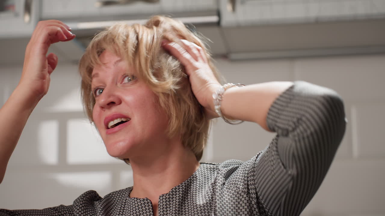 Beautiful housewife smiles warmly while singing and gently touching her short bob hair, radiating happiness and charm inside bright modern kitchen with cozy atmosphere and stylish decor