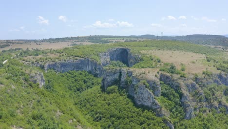 Approaching-drone-shot-revealing-the-entrance-of-Prohodna-cave,-where-two-large-openings-inside-its-chambers-are-famously-called-God's-Eyes,-located-in-Karlukovo,-Bulgaria