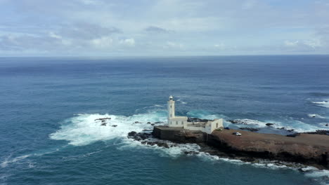 las olas chocando contra la costa rocosa con el faro de dona maria pia, farol da praia en la isla de santiago, cabo verde. - fotografía aérea