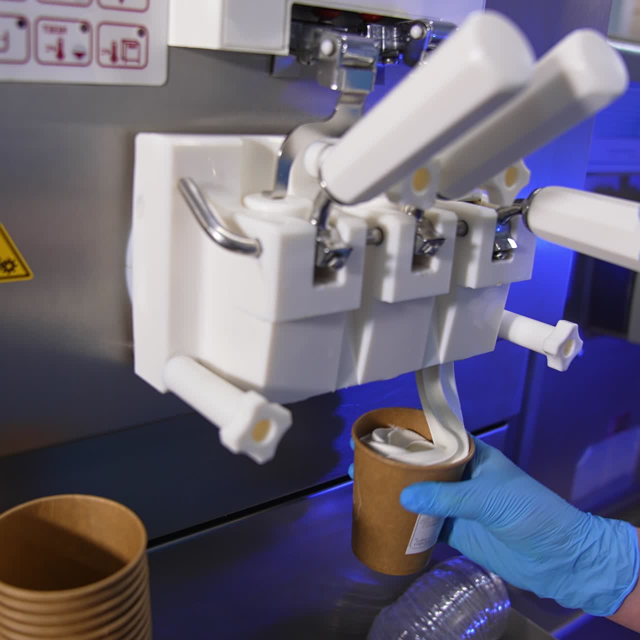 White soft vanilla ice-cream is poured from an automatic machine. Sweet dessert is packed into a paper cup