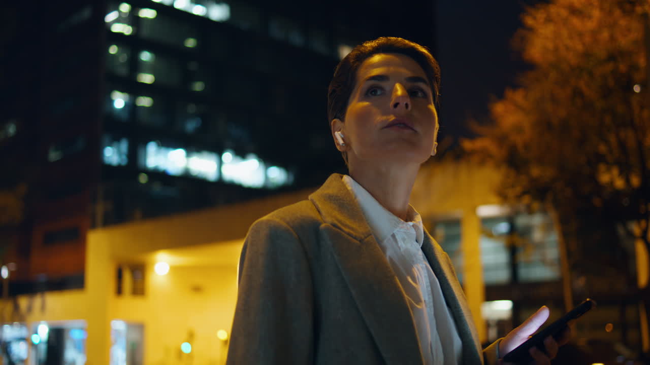 una mujer exitosa caminando sola por la ciudad nocturna. una mujer de negocios relajada escuchando música.