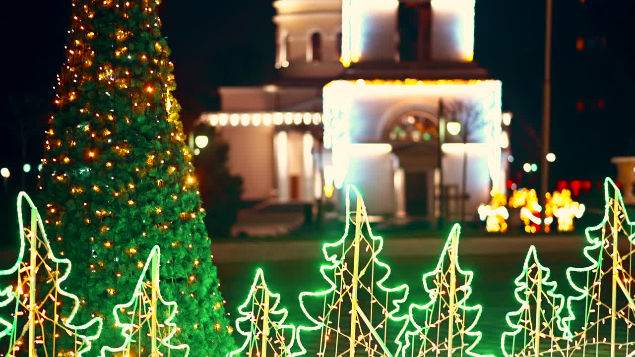Colorful holiday lights decorate the park, creating a joyful atmosphere. A Christmas tree stands tall next to a brightly lit church, enchanting visitors during the winter night