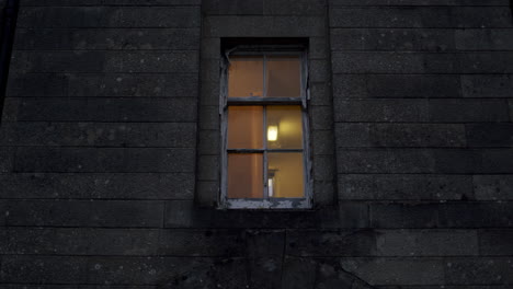 wooden window with the light shining in apartment on a grey brick wall of a building, handheld urban location