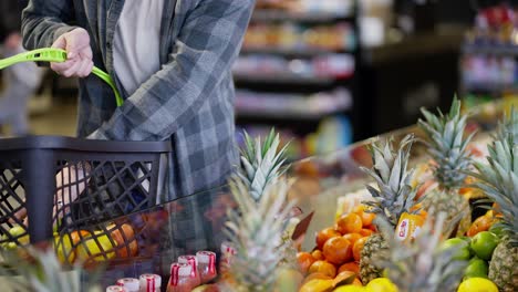cerca de un cliente del supermercado en una camisa a cuadros selecciona la fruta que necesita entre los frutos de mango naranja y piña en el supermercado