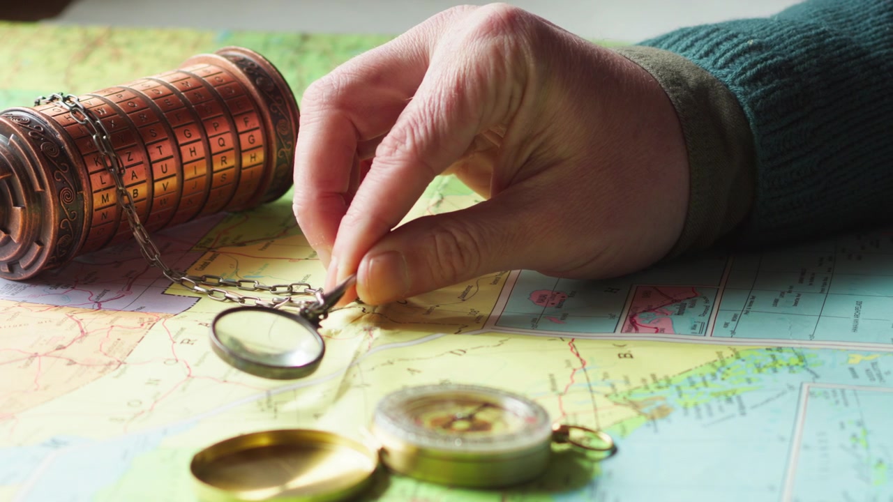 Close-up of a hand using a magnifier over a detailed map with a compass and cryptex, suggesting treasure seeker investigation, navigation, and decoding hidden clues.
