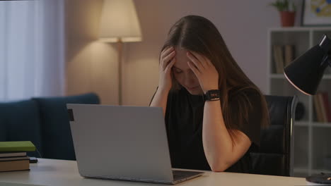 mujer sobrecargada de trabajo está frotando las sienes durante el trabajo con la computadora portátil en casa por la noche dolor de cabeza y exceso de fatiga del trabajador de oficina y freelance