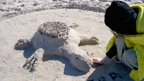 a sand turtle on the beach being built by a girl in a hood