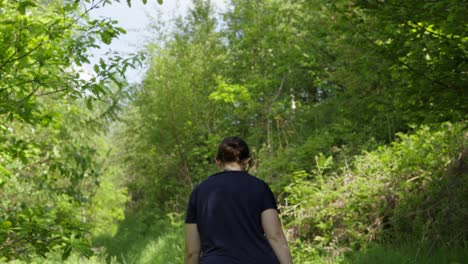 Low-Angle-Tracking-View-of-Lone-Woman-Walking-on-Path-in-Forest-on-Summer-Day