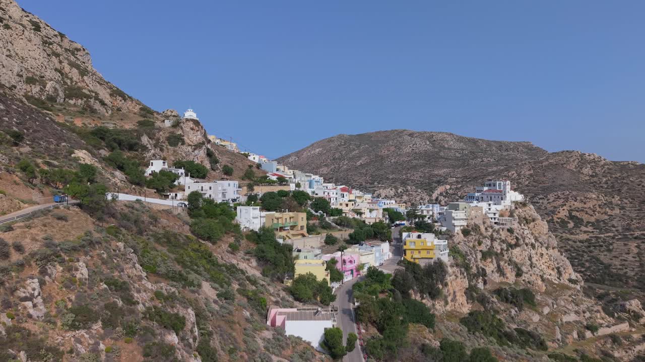 Drone approaching Menetes Village on Karpathos Island, Greece — revealing its location, colorful traditional houses, and scenic Mediterranean landscape