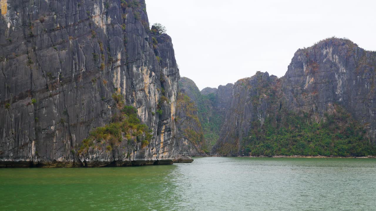 Towering limestone karsts with sheer cliff faces rise dramatically from the emerald-green waters of Ha Long Bay, mesmerizing seascape, ancient rock formations meet the tranquil Vietnamese gulf waters