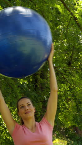 mujer en forma levantando una pelota de ejercicio en el parque