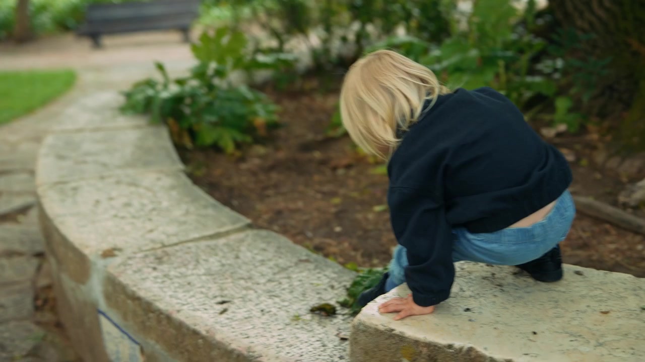 Bambino piccolo che esplora un parco e si siede su un muretto di pietra