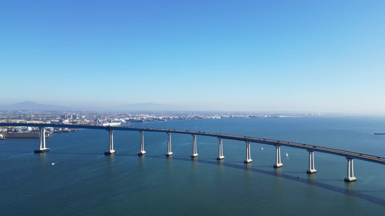 A drone shot capturing the San Diego Coronado Bridge from a distance, with scenic views of the bay and city.