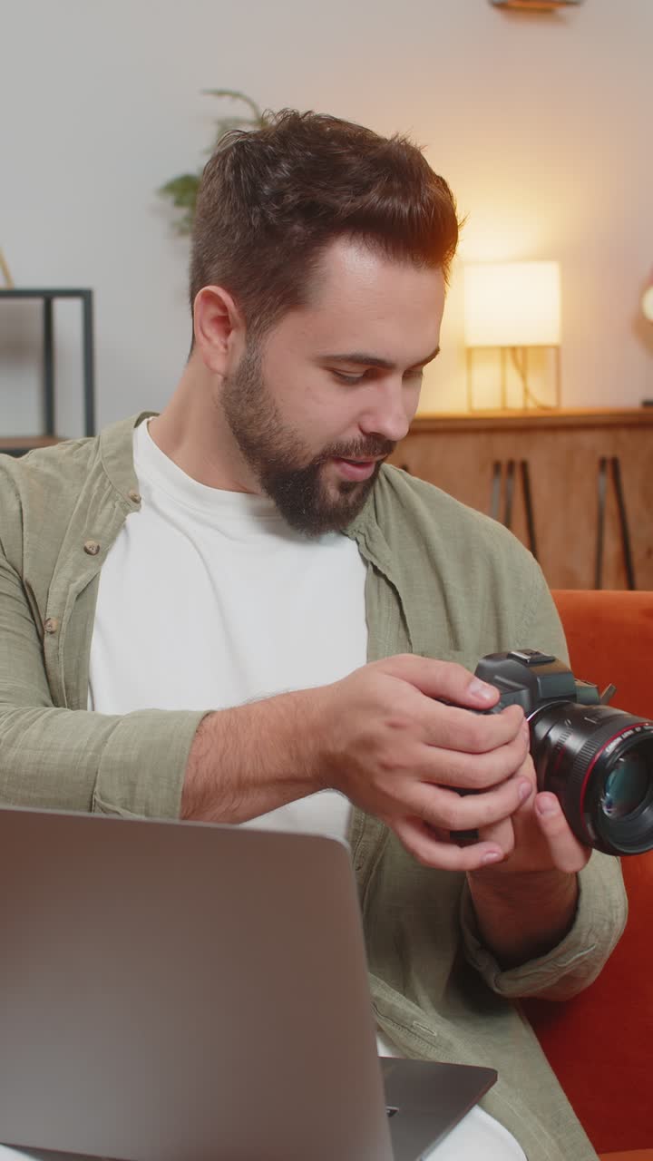 Happy man photographer with laptop holding digital camera looking at screen choosing photos at home