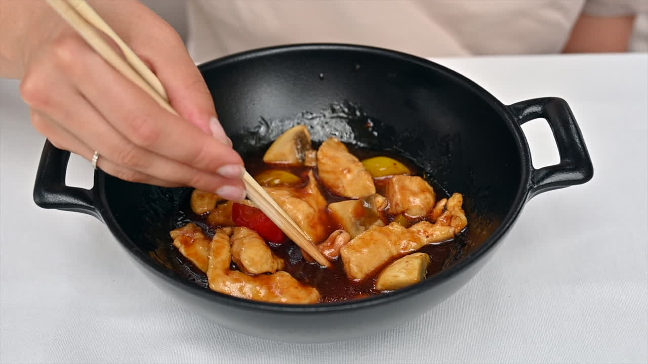 Woman eating chicken with vegetables and sweet sauce in a black pan at a chinese restaurant