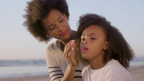 loving mother brushing the crumbs off her daughter's face while little girl eating croissant during a picnic on the beach