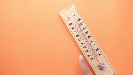 hand pointing at a wooden thermometer on an orange background