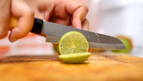 manos de mujeres usando un cuchillo cortaron la cal verde en pedazos en una tabla de madera en una cocina