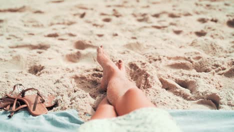 First-person-view-of-a-woman-relaxing-in-the-beach-while-stretching-his-legs-in-the-sand,-pov-of-a-tourist-during-summer-vacations