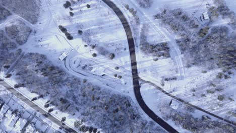 birds eye view aerial drop in height in a winter town with light traffic and a park next to a highway