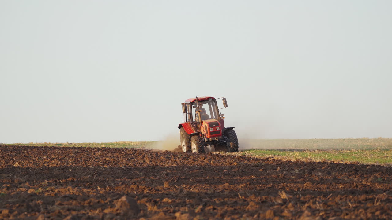 Tractor plowing fields, preparing land for sowing. Farmer in tractor preparing land in farmlands outdoors. Agricultural industry.