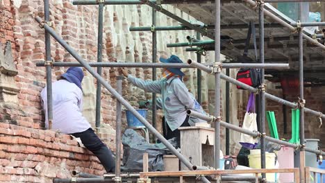 workers meticulously repairing brickwork on scaffolding.