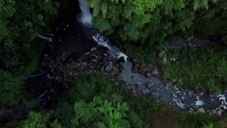 Una-Toma-De-Drones-De-Un-Arroyo-Que-Fluye-Salvaje-Pasando-Piedras-Grises-En-Forma-De-Bola-Rápida-Y-Hojas-De-Hierba-Verde-Cerca-De-La-Cascada-Kedung-Kayang,-Magelang,-Java-Oriental,-Indonesia