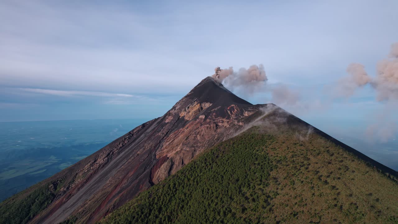 A breathtaking drone shot captures the active Volcán de Fuego in Guatemala, with a plume of ash and gas rising from its summit