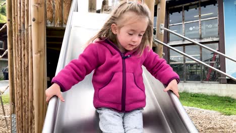 cute young little girl sliding down a slide in slow motion with mountains in the background