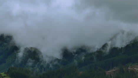 drone shot of rain clouds moving over heavily forested mountain range, new zealand