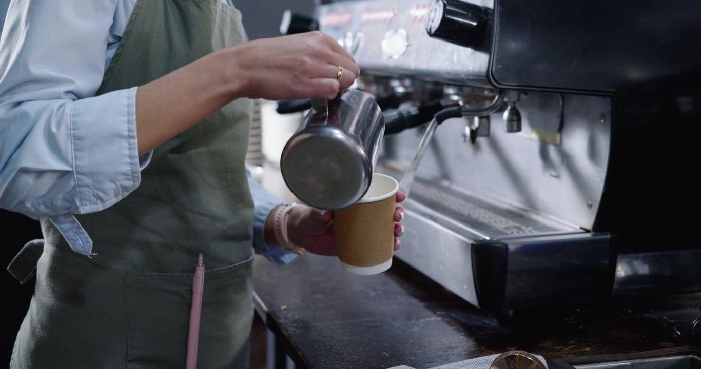 Un barista sta attivando la macchina da caffè espresso, estraendo un caffè, montando e versando il latte per completare la bevanda.