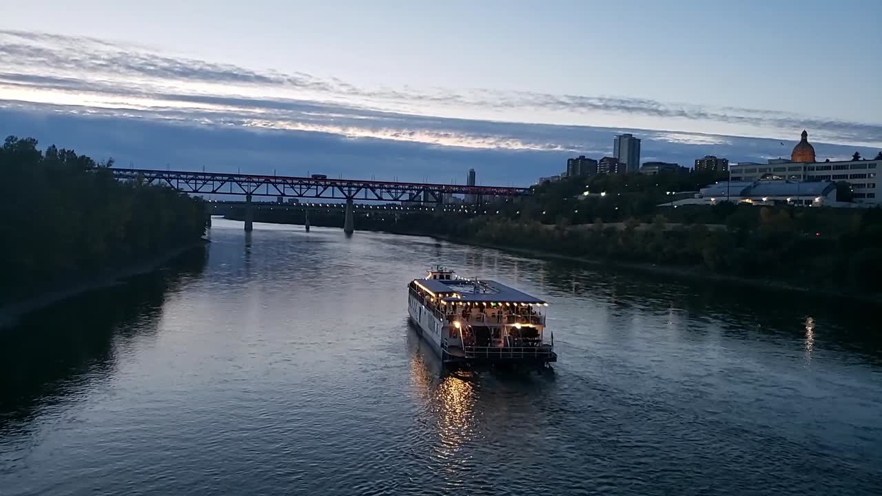 TIME LAPSE North Saskathchewan River Boat dining party on a summer evening inbetween the Water Dale Bridge and the High Level Bridge in downtown Edmonton Canada with a blue gradaition sky