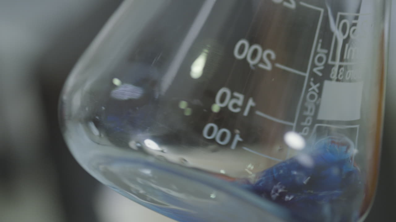 Close-up of a laboratory flask with a liquid substance stirring or reacting, in a controlled environment.