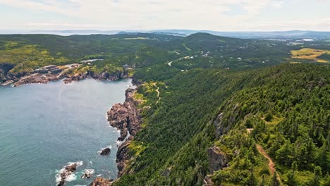 a drone soars over red cliff's rolling hills and farmland, revealing dramatic coastal cliffs dropping into the blue atlantic and lush forests