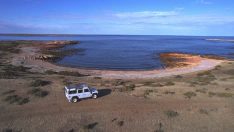 Kreisförmige-Drohnenansicht,-Die-Die-Bucht-Mit-Dem-Auto-Und-Die-Wunderschöne-Umgebung-Am-Strand-Von-Bahia-Bustamante-Freigibt