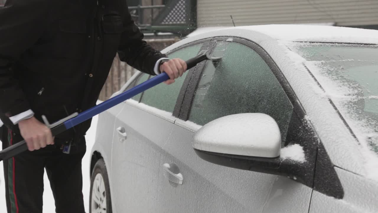 hombre vestido con chaqueta negra quitando hielo en la ventana de su auto durante el día de invierno - toma de primer plano