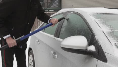 man wearing black jacket removing ice on his car window during winter day - closeup shot