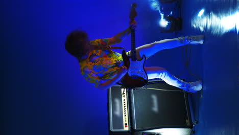 vertical video cheerful man jumping dancing and playing guitar in colored neon light smoke and spotlights in the studio on a changing background