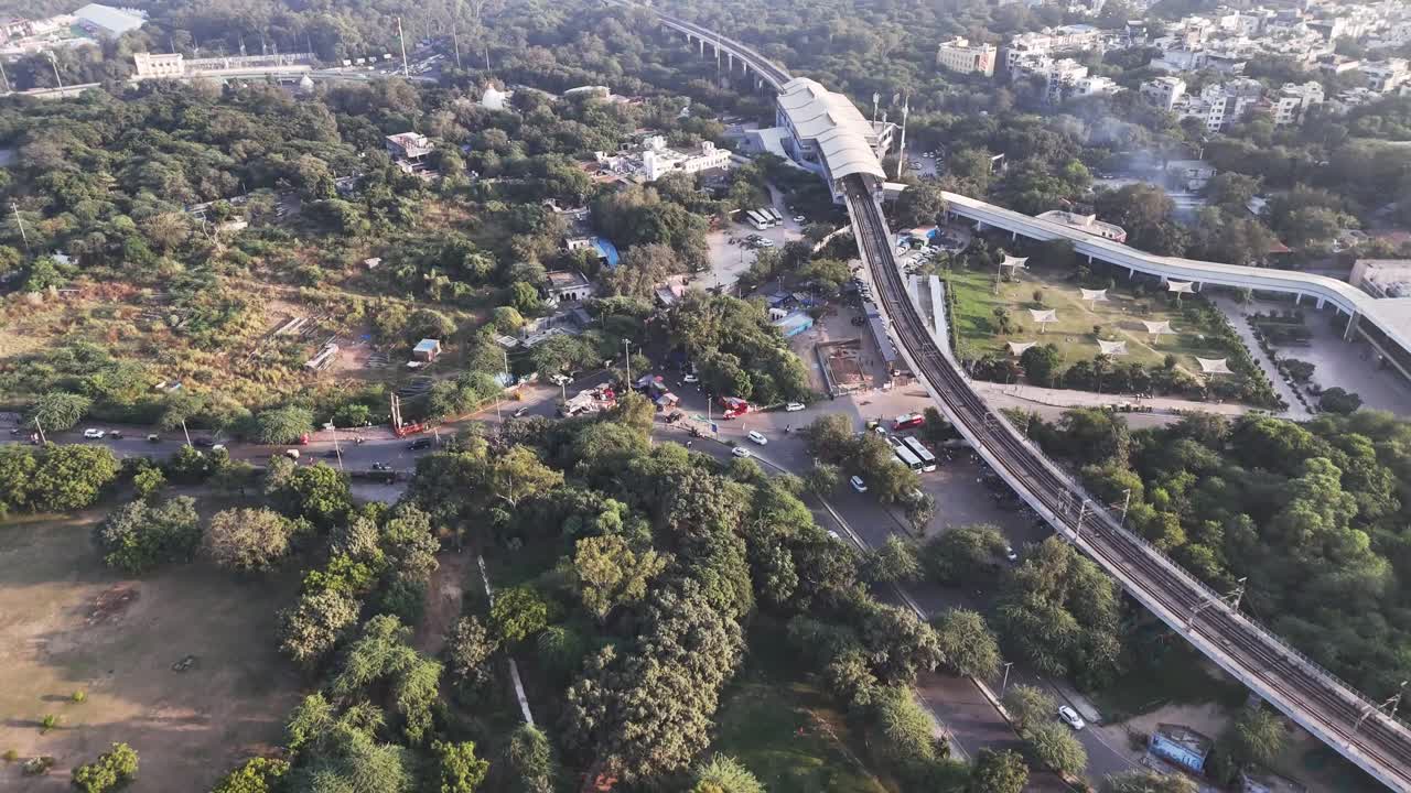 Vista aerea della stazione della metropolitana di Nehru Place, Nuova Delhi, che mostra i binari sopraelevati della metropolitana di Delhi che attraversano una fitta vegetazione, trafficati incroci stradali e i quartieri urbani circostanti a sud di Delhi