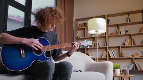 young curly musician with a blue guitar. a very tired, irritated young guitarist in a living room. fail. disappointment.