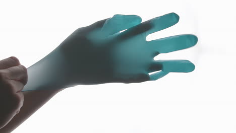 woman's hand against a bright white background applying a blue latex glove in slow motion