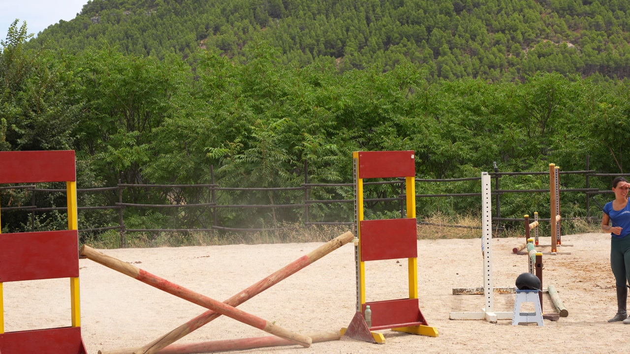 Trainer riding horse shows student how to jump accurately over hurdle at equestrian center
