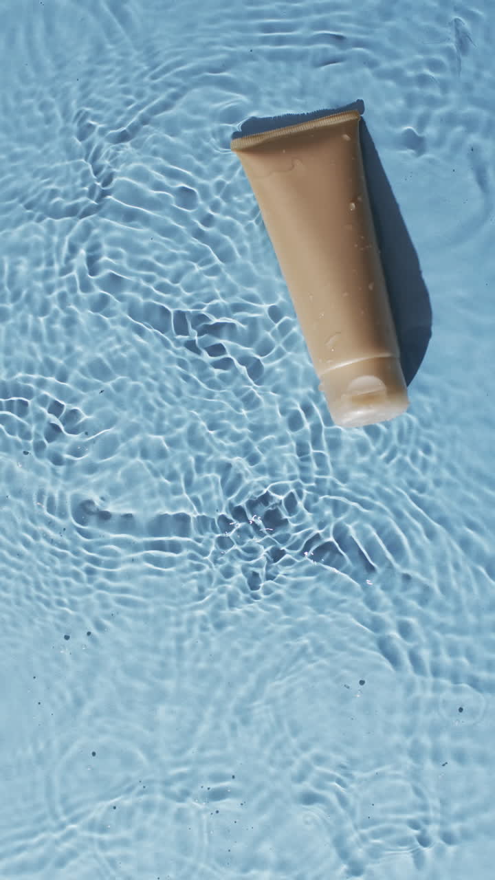 Vertical video of beauty product tube in water with copy space on blue background