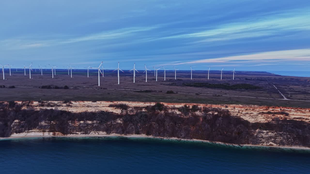Vindmøller står nær klipper ved kysten i det sene eftermiddagslys