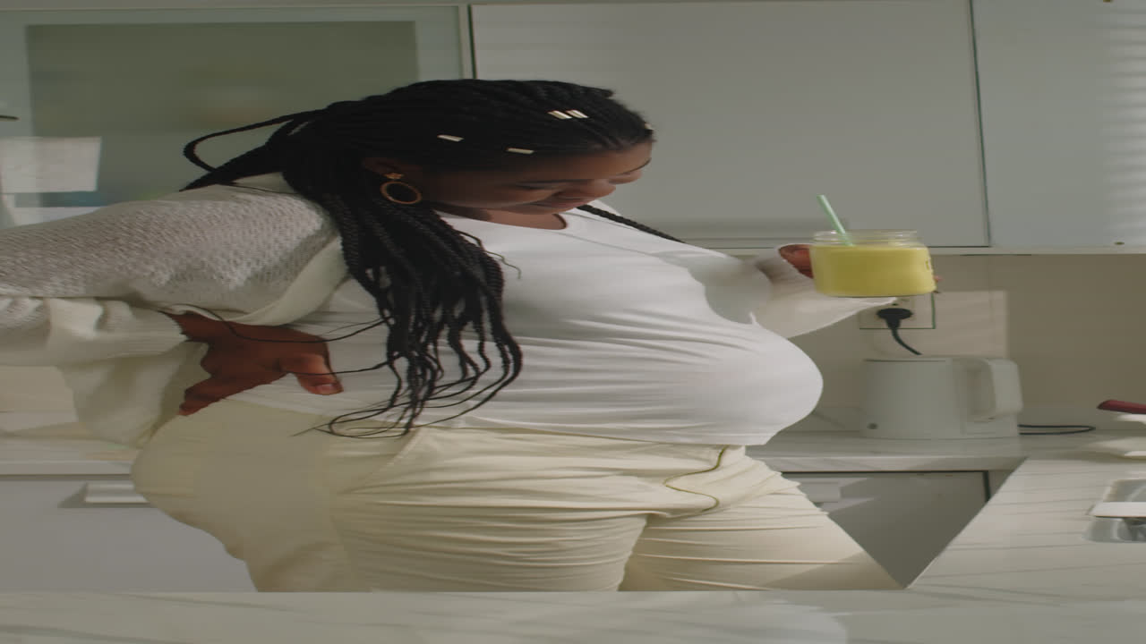Pregnant woman drinking a smoothie in the kitchen