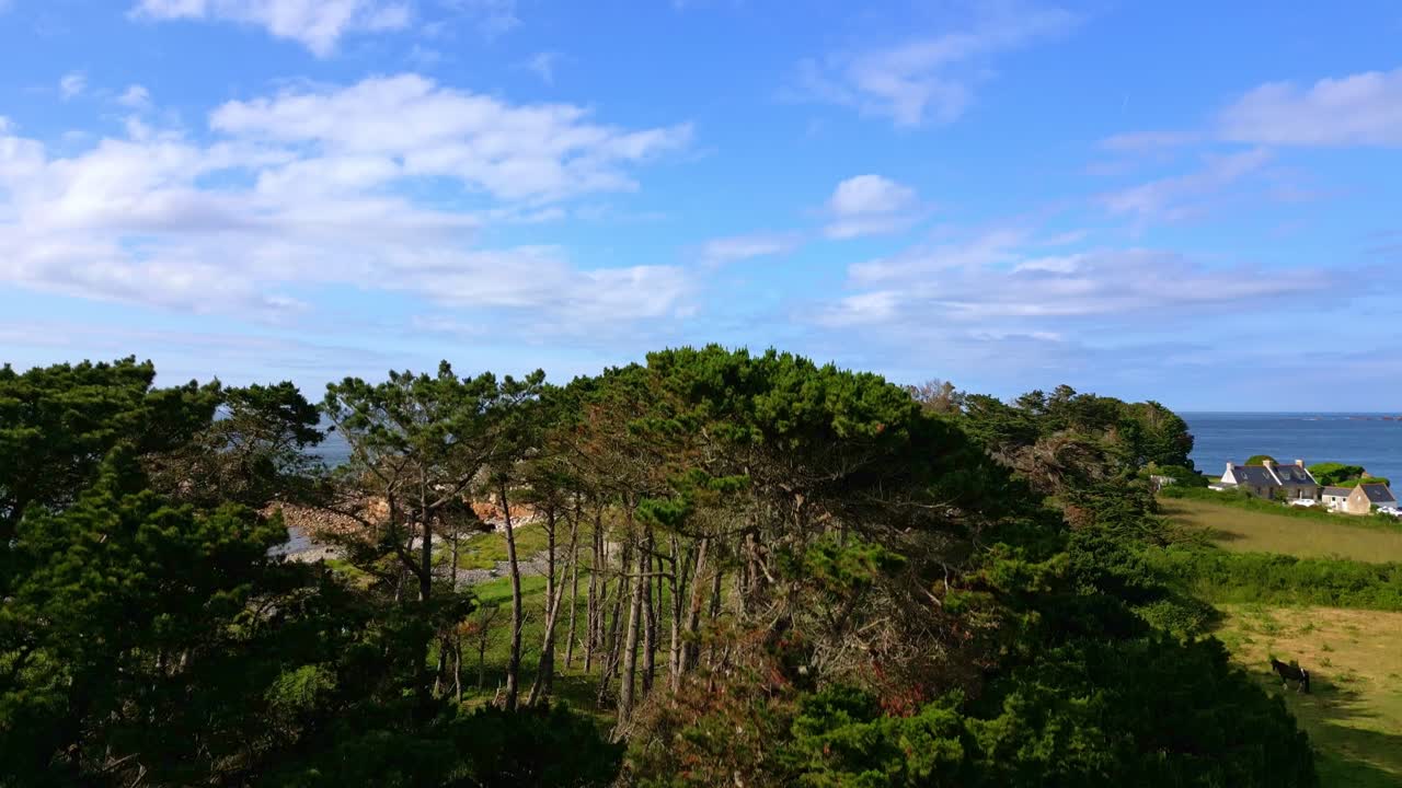 Upward drone movement near a rocky islet settlement connected to coastline by a narrow beachside, Côte de Granit Rose, Brittany, France.